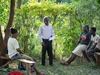 Paul Andasi for Practical action standing outdoors with a group of people having a discussion, Kenya, 2024.