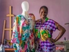 A young fashion designer standing beside a brightly coloured dress she designed, for Jobberman, Nigeria, 2024.