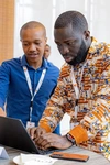 Two young men in brightly coloured button up shirts working on a laptop together on Day 1 of the Baobab Summit 2025