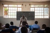 Teacher stands at the front of a classroom of students with a blackboard behind him