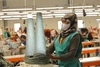 Woman working in a textile factory with a medical facemask wearing a green working vest