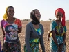 A group of young women standing outdoors in a field wearing brightly coloured casual clothing and headscarves, Dagana and Richard Toll, Senegal, 2024.