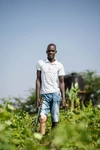 James Esinyen standing in a farm field in a white t-shirt and jeans
