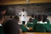 A teacher stands in front of a blackboard educating a group of students in green shirts