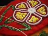 Beadwork craft of a flower with red, white, yellow and green glass beads on a red fabric