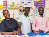 Victoria and two of her employees smiling together, behind the counter at her healthcare clinic, in Gurei, South Sudan 2026.