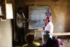 A woman from the Tuugane Microcredit Group stands at the board at the front of the classroom. 