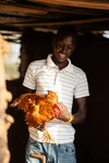 James standing in a chicken coop holding onto a brown chicken and smiling