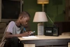 Young boy sat at a desk writing with a radio in front of him