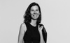 Black and white image of Jennifer Fonstad smiling to camera with her jacket over her shoulder