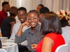 Two young women engaged in conversation at a table in a busy conference room, Mastercard Foundation Associates Program, Accra, Ghana.