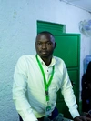 James Gihoma Ntakiruti, Executive Director of YIDA Youth Initiative, wearing a white button up shirt with a green lanyard. YIDA is a refugee-led organization based in Uganda's Kyaka II refugee settlement.