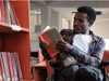 A man sitting in a wheelchair in a library, reading a book.