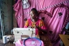 A woman sitting behind a sewing machine with bright pink fabric behind her.