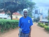 Joyce Apayi, standing outdoors in a blue sweater smiling