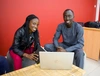 Two people smiling as they work on a laptop.