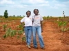 Two young Mastercard Foundation Scholars at EARTH U, standing outdoors in a field, smiling brightly, wearing casual clothing 4x3.