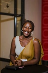 A woman smiling joyfully wearing a white top with a gold coloured sash