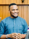 Great Nnamani talking and smiling wearing a light blue button up shirt with a white pattern along the front and pocket 
