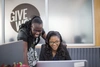 Two women smile as they look at a computer screen.