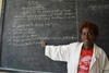  Marcelline Uwizeyimana smiling to camera pointing to a blackboard