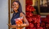 A young woman standing outdoors holding a large bag of fresh tomatoes holding a cell phone, Big Samps, Ghana, 2024.