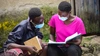 Two people reading together wearing facemasks