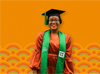 Ibukunoluwa Omotola standing in graduation cap and sash with an orange dress underneath
