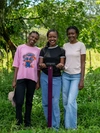 Two young Mastercard Foundation Scholars at EARTH U, standing outdoors in a field, smiling brightly, wearing casual clothing.