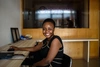 A student smiling while sitting at a desk in front of a laptop