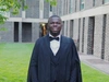 Theophilus Adu-Gyamfi smiling in his graduation cap and gown standing outdoors.