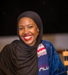Murungi Sarah in a black headscarf and grey and bright blue patterned robe, with an ALU scarf in their brand colours of blue, red and white