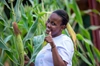 Woman giving a thumbs up to the camera in a field surrounded by tall plants.