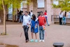 Two young male visually impaired students using mobility sticks and being assisted to walk through an outdoor courtyard