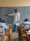 A teacher in a classroom, pointing at the blackboard.