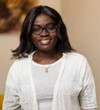 Claudine Mendy wearing a white lace style cardigan with a white top, and black rimmed eye glasses