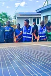 Vasco Hamisi co-founder of Okapi Green, wearing a blue vest and speaking to a group of people over a large solar panel