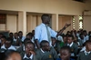 A teacher standing among seated students in uniform, giving a lesson in a classroom