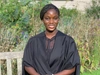 Lilian Amponsaa Boateng wearing a black graduation gown sitting on a wooden bench outdoors