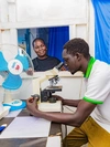 Victoria overseeing her employee, who is looking through a microscope at her healthcare clinic, in Gurei, South Sudan 2026.