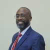 Adrian Bukenya smiling to camera dressed in a smart blue suit and red tie