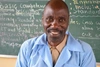 Man smiles to camera with a blackboard in the background 