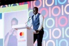 Bior Ajak stands in front of a podium in a smart outfit, addressing the crowd at the Baobab Summit in 2022.