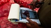 A close up image of hands, holding a receipt notebook and a smartphone, working on onion pricing on the online Soko Kijiji store.