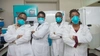 Four healthcare workers standing with arms crossed in white lab coats wearing protective masks