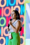 Young woman standing on stage at Baobab Summit 2022 wearing a white top with smart bright green business pants, holding a microphone
