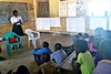 Group of young children sat in a classroom listening to a teacher talking 