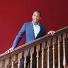 Philibert Adankon smiling to camera stood on stairs wearing a smart blue suit