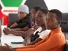 A group of young people sitting at a desk, listening to a lesson in a classroom, Ajira, Kenya, 2024.