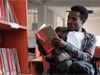  Man reading a book in a library while sitting in a wheelchair.